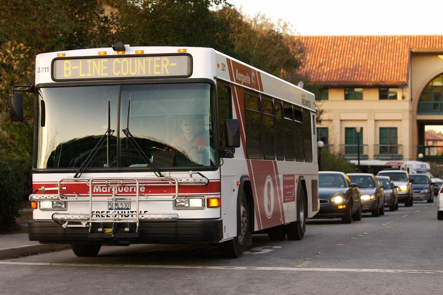A red and white bus is driving towards us on Stanford campus.