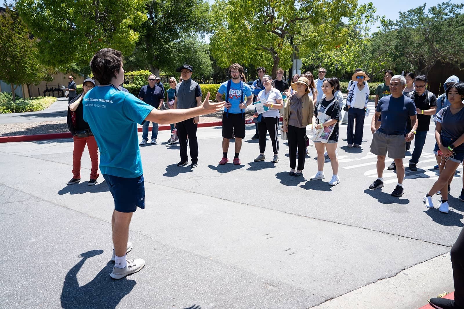 A student in a blue shirt with their arms outstretched faces a tour group of people, talking animatedly. 
