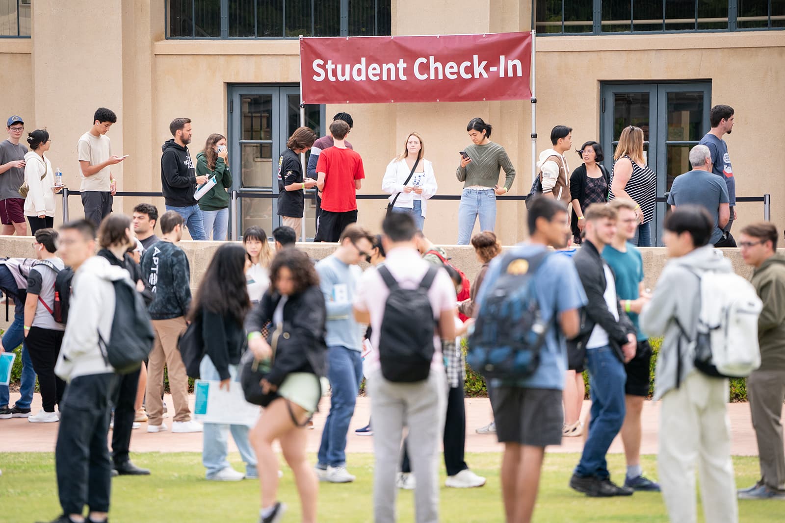 Students gather on the grass in front of the student check-in at a building on campus.