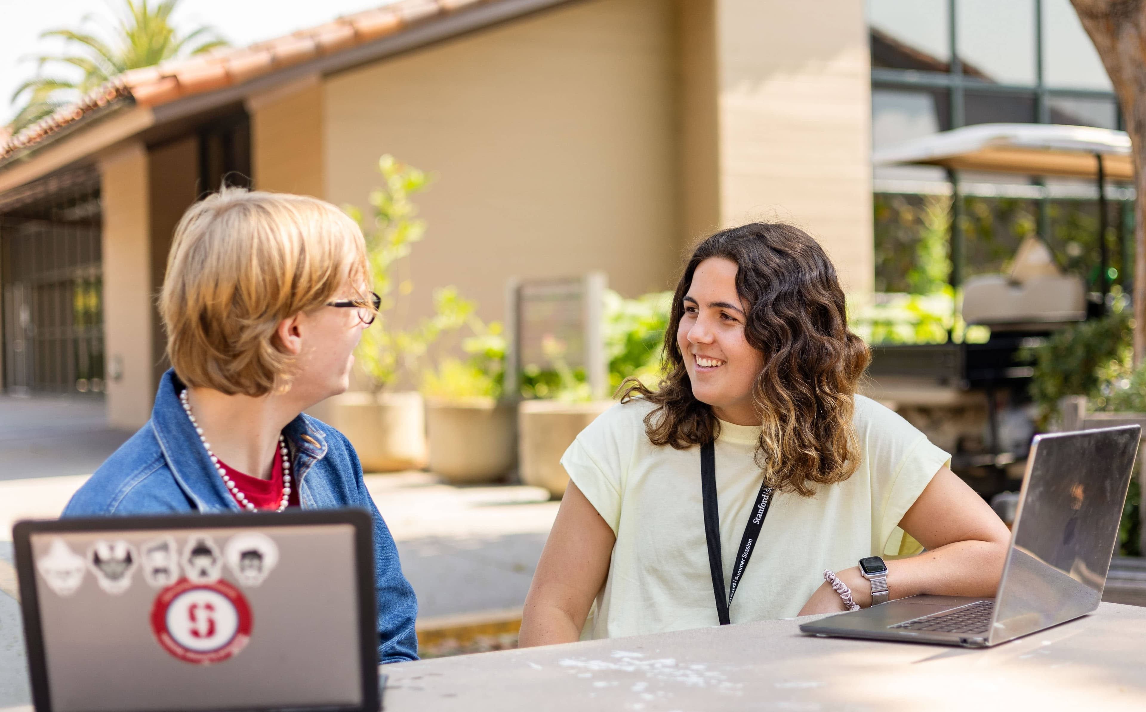 Two students talk with a laptop in the foreground.