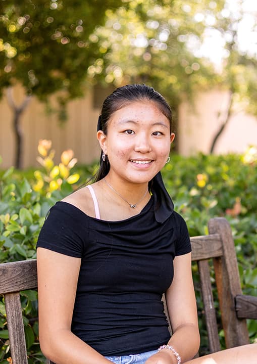 Ann sits outside on a bench in a black top.