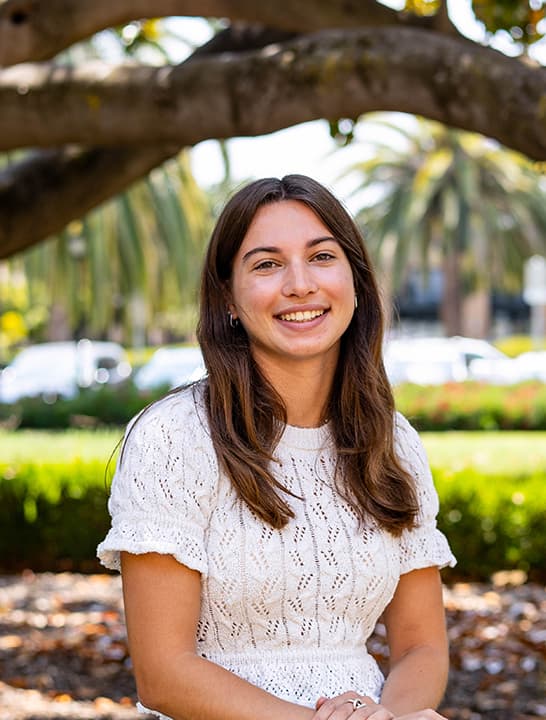 Clara sits outside in a white top.
