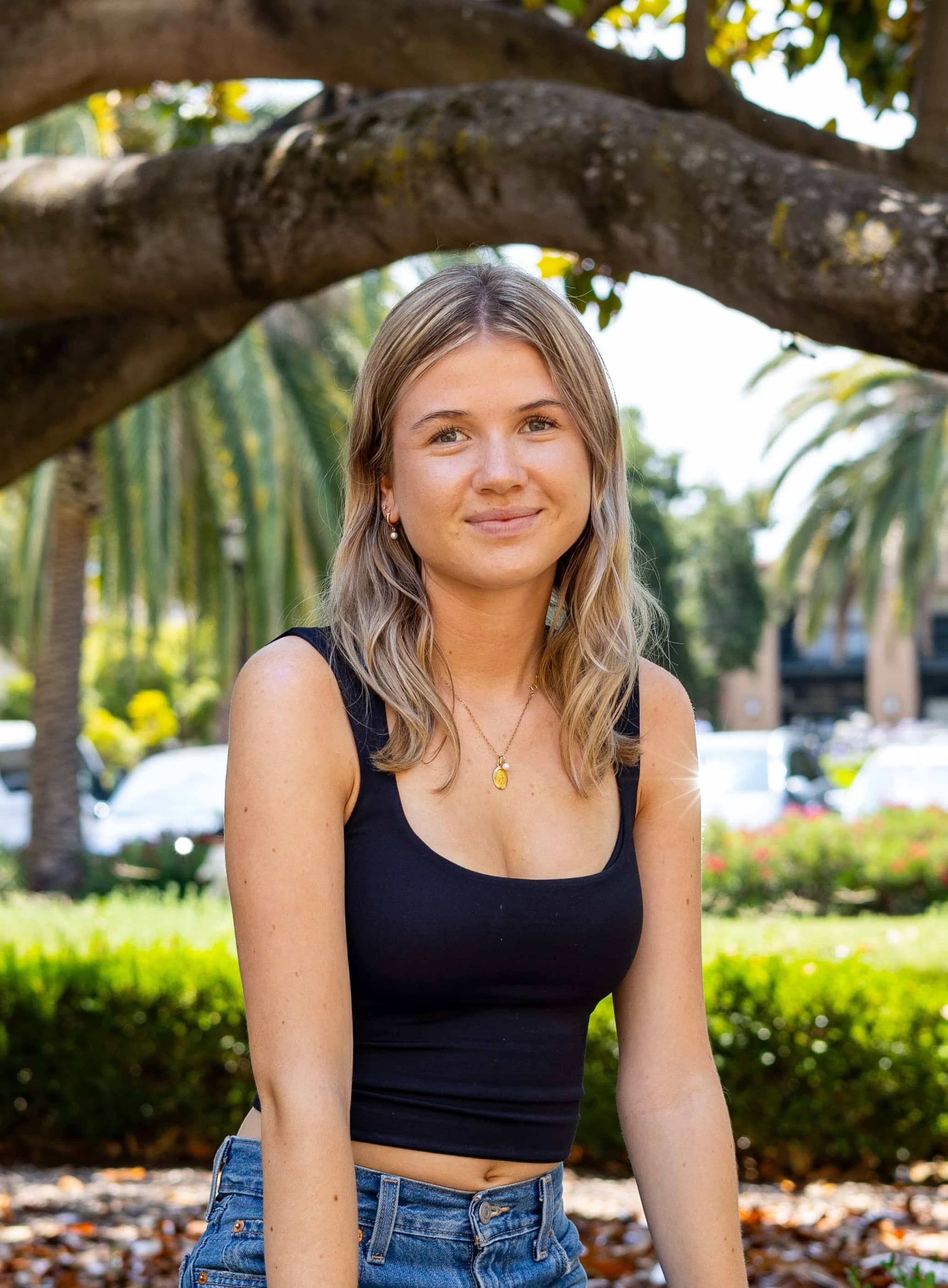 Helena wears a black top and sits under a tree.