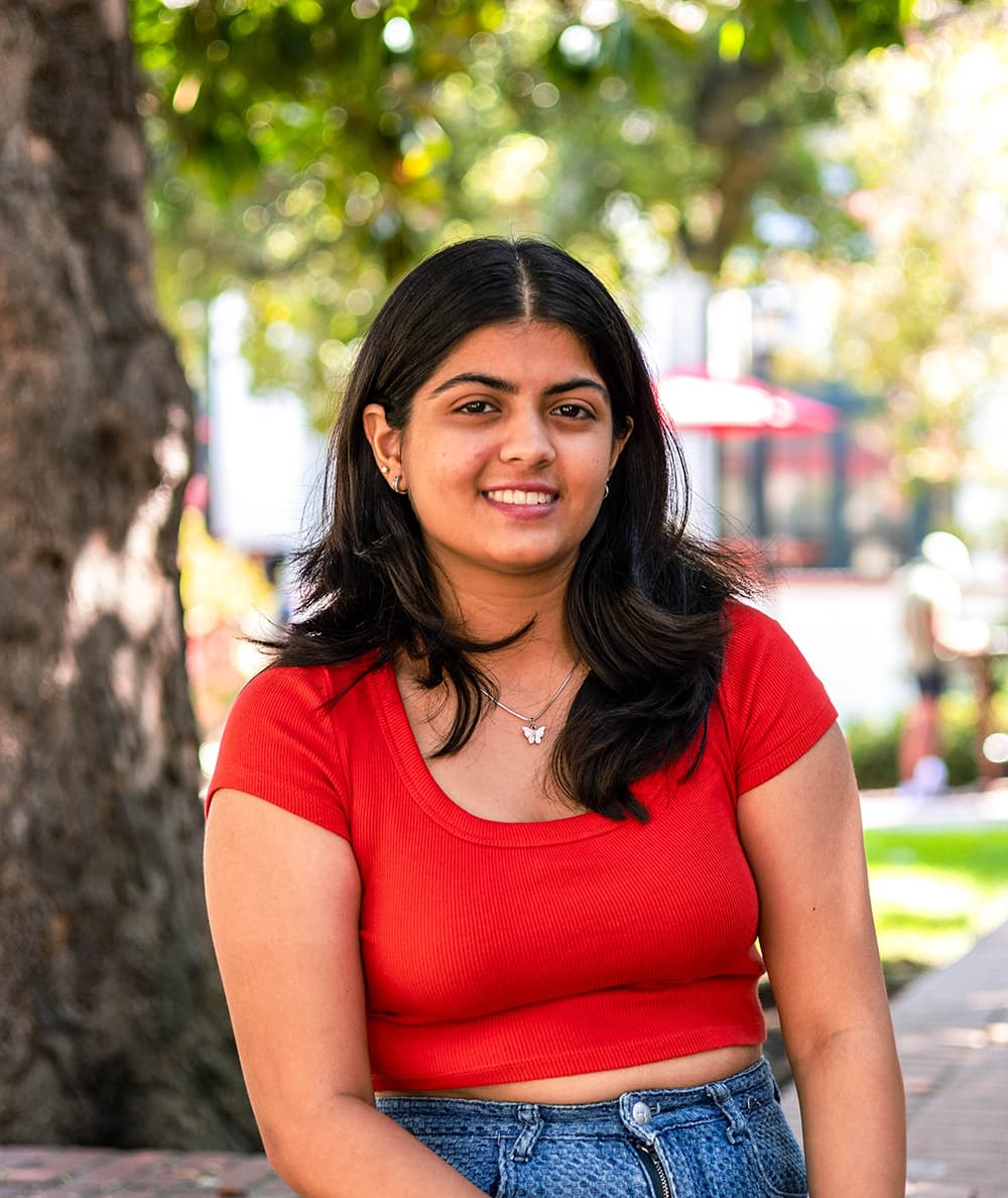 Gunjan sits outside wearing a red top and smiling.